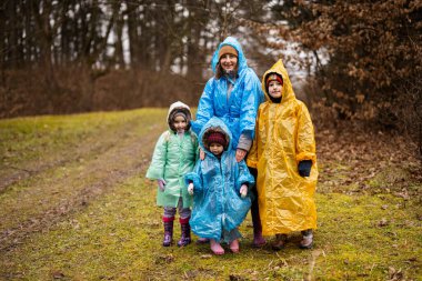 Mother and three children in the forest after rain in raincoats together.