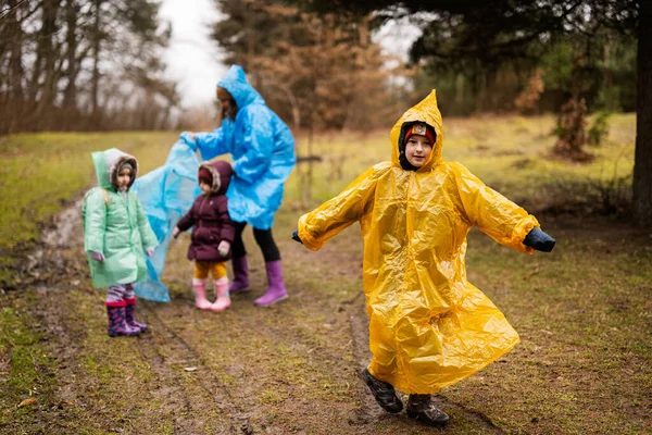 Boy in yellow raincoat against mother and children in the forest after rain in raincoats together.