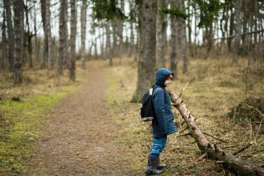 Boy with backpack and rain boots in the forest.