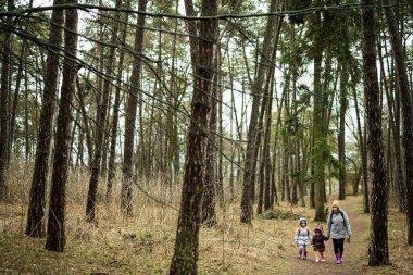 Mother and two daughters with backpacks walking along the forest road together.