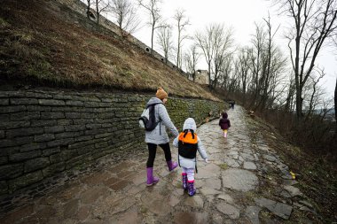 Mother and children walk up the wet path to an ancient medieval castle fortress in rain.