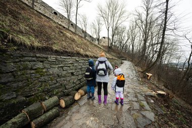 Mother and children walk up the wet path to an ancient medieval castle fortress in rain.