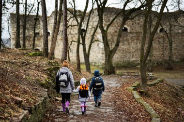 Back of mother and kids walk path to an ancient medieval fortress in rain. Terebovlia castle, Ukraine.