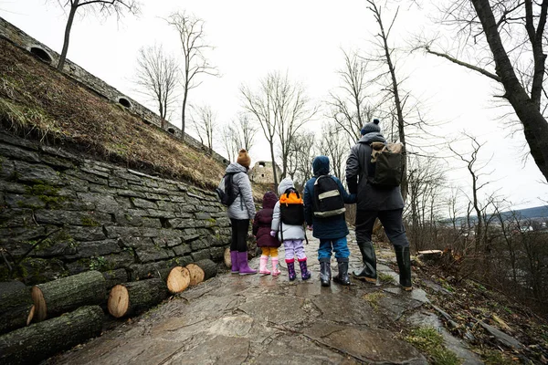 Back of family with three children stand on wet path to an ancient medieval castle fortress in rain.