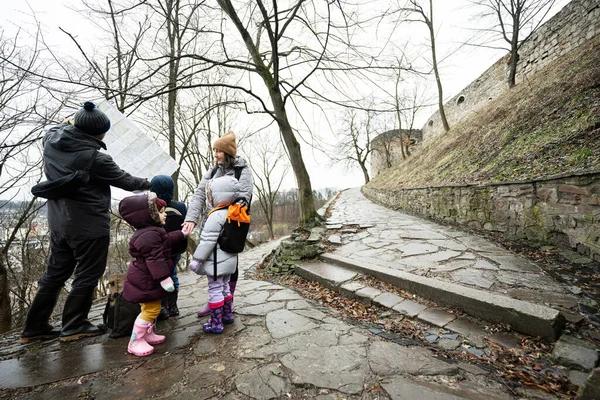 Family tourist look at map with three children, stand on wet path to an ancient medieval castle fortress in rain.