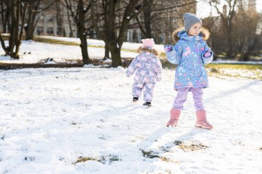 Two sisters in winter snowsuit playing together in sunny day.
