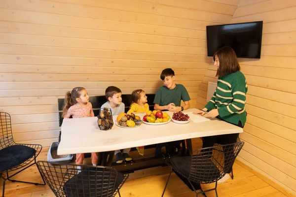 Mother with four children eat fruits in wooden country house on weekend.