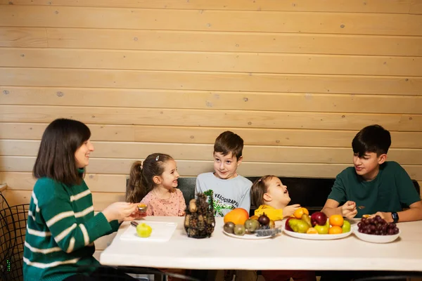 Mother with four children eat fruits in wooden country house on weekend.