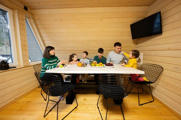 Family with four kids eat fruits in wooden country house on weekend.