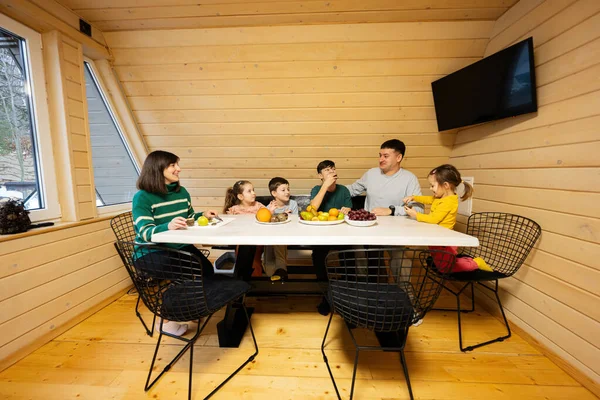 Family with four kids eat fruits in wooden country house on weekend.