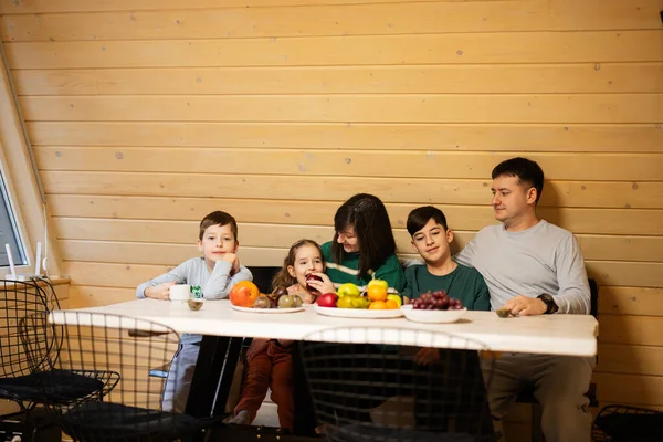 Family with three kids eat fruits in wooden country house on weekend.
