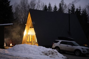 Modern üçgen kulübesinin alacakaranlıkta, dağlarda şenlik ateşiyle ve park halindeki SUV arabasıyla..