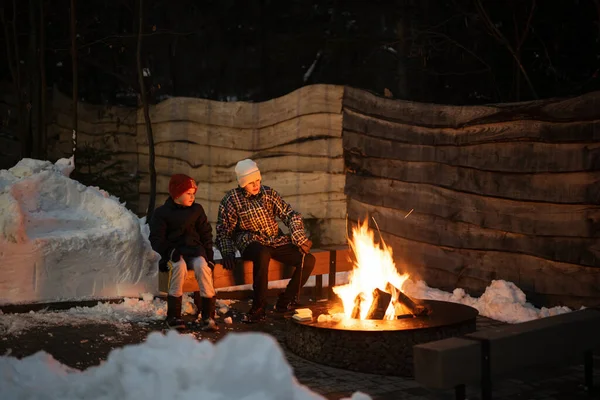 Two brothers sit by the fire pit in winter night.