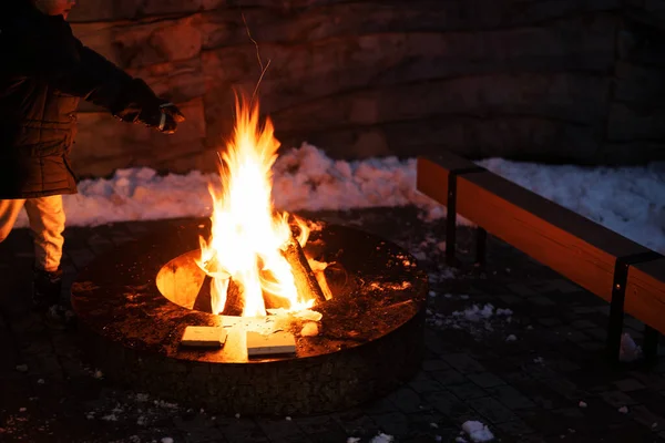 Boy warm his hands by the fire pit in winter night.