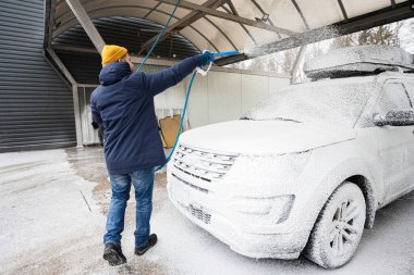 Man washing american SUV car with roof rack at a self service wash in cold weather.