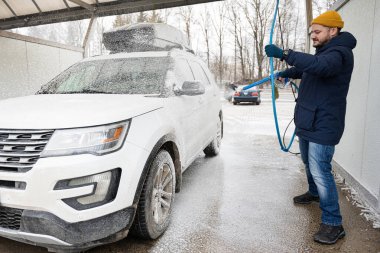 Man washing american SUV car with roof rack at a self service wash in cold weather.