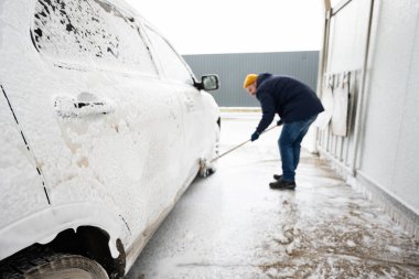 Man washing american SUV car with mop at a self service wash in cold weather.