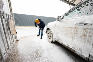 Man washing american SUV car with mop at a self service wash in cold weather.