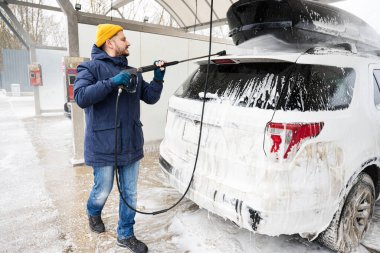 Man washing american SUV car with roof rack at a self service wash in cold weather.