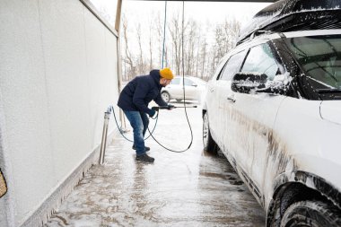 Man washing high pressure water american SUV car with roof rack at self service wash in cold weather.