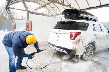 Man washing high pressure water american SUV car with roof rack at self service wash in cold weather.