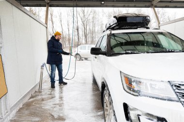 Man washing high pressure water american SUV car with roof rack at self service wash in cold weather.