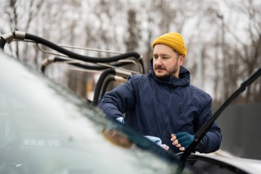 Man wipes american SUV car windshield with a microfiber cloth after washing in cold weather.