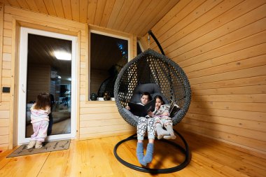 Erkek ve kız kardeşi rahat asılı sandalyede kitap okuyorlar. Küçük ahşap kulübede. Kırsal kesimde hayat.