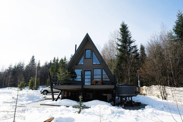 Wooden triangle country tiny cabin house with hot tub spa and suv car with roof rack in mountains. Soul weekends.