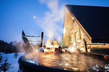 Aile, kulübenin terasında tahta fıçı jakuzide yıkanmayı seviyor. Odun ve sıcak su yakmak için şöminesi olan İskandinav küveti..