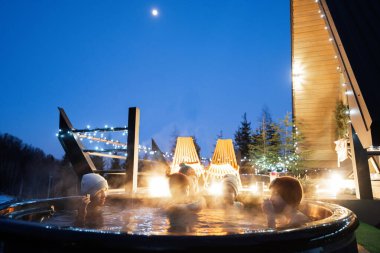 Aile, kulübenin terasında tahta fıçı jakuzide yıkanmayı seviyor. Odun ve sıcak su yakmak için şöminesi olan İskandinav küveti..