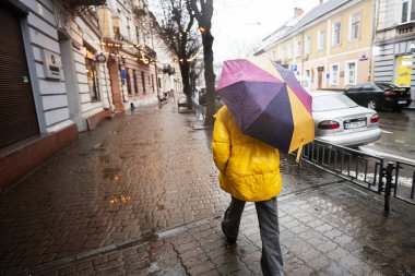Ivano-Frankivsk, Ukrayna - Mart 2023: Sarı elbiseli kadın yağmur sokağında yürüyor.
