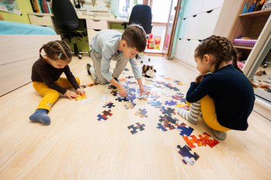 Children connecting jigsaw puzzle pieces in a kids room on floor at home.  Fun family activity leisure. 