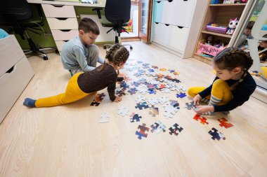 Children connecting jigsaw puzzle pieces in a kids room on floor at home.  Fun family activity leisure. 