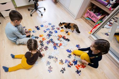 Children connecting jigsaw puzzle pieces in a kids room on floor at home.  Fun family activity leisure. 