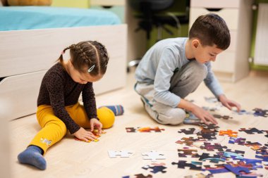 Children connecting jigsaw puzzle pieces in a kids room on floor at home.  Fun family activity leisure. 