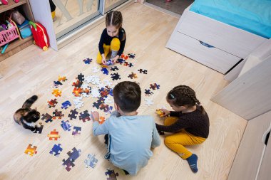 Children connecting jigsaw puzzle pieces in a kids room on floor at home.  Fun family activity leisure. 