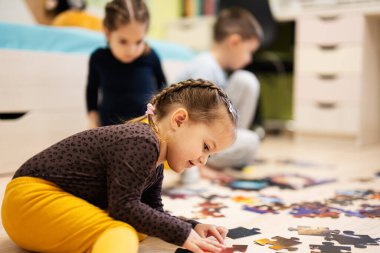 Children connecting jigsaw puzzle pieces in a kids room on floor at home.  Fun family activity leisure. 