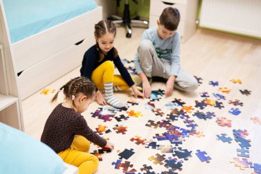 Children connecting jigsaw puzzle pieces in a kids room on floor at home.  Fun family activity leisure. 
