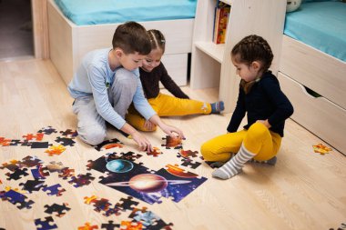 Children connecting jigsaw puzzle pieces in a kids room on floor at home.  Fun family activity leisure. 