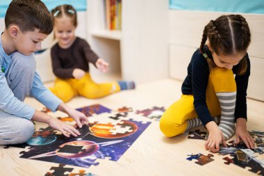 Children connecting jigsaw puzzle pieces in a kids room on floor at home.  Fun family activity leisure. 