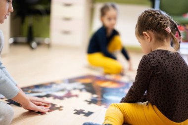 Children connecting jigsaw puzzle pieces in a kids room on floor at home.  Fun family activity leisure. 