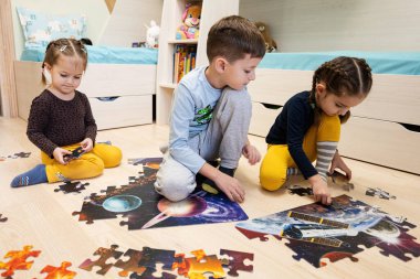 Children connecting jigsaw puzzle pieces in a kids room on floor at home.  Fun family activity leisure. 