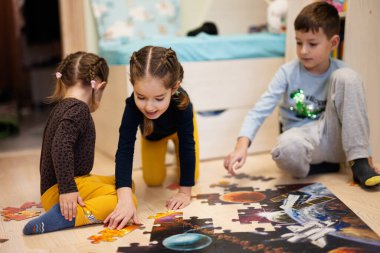 Children connecting jigsaw puzzle pieces in a kids room on floor at home.  Fun family activity leisure. 