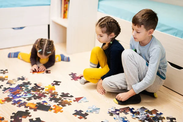 Children connecting jigsaw puzzle pieces in a kids room on floor at home.  Fun family activity leisure. 