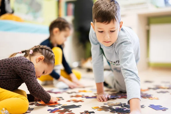 Children connecting jigsaw puzzle pieces in a kids room on floor at home.  Fun family activity leisure. 