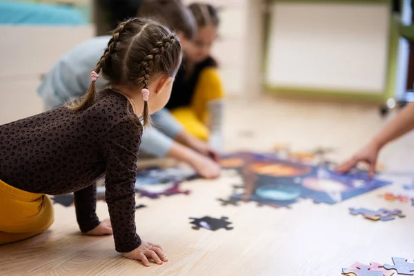 Children connecting jigsaw puzzle pieces in a kids room on floor at home.  Fun family activity leisure. 