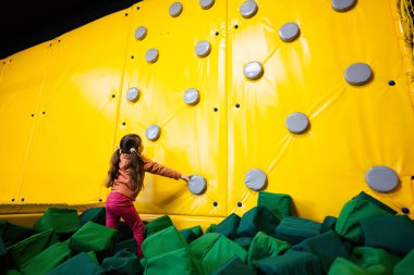Sarı çocuk parkında duvara tırmanan küçük bir kız. Etkin gösteriler sırasında hareket halindeki çocuk.