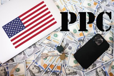 PPC. Klik başına ödeme konsepti. ABD bayrağı, anahtarlı dolar parası, dizüstü bilgisayar ve telefon geçmişi.