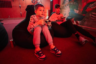 İki erkek oyuncu kırmızı oyun odasında oyun konsolu oynuyorlar..